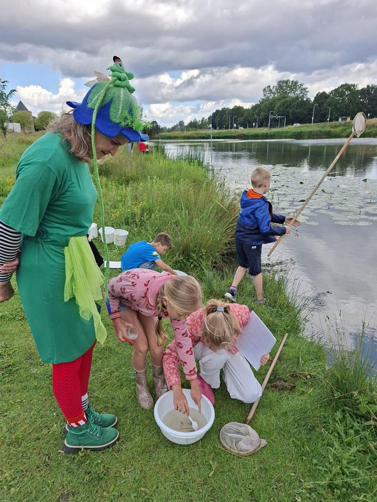 Juf Kikker met kinderen aan de waterkant, op zoek naar waterdiertjes